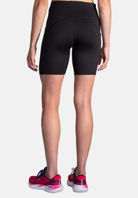 Shorts de sport noirs taille haute au design ajusté. Tissu lisse, longueur mi-cuisse, avec poches latérales et détails de couture contrastés.