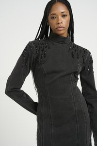 Svart denimkjole med lange ermer, høy krage, pyntede skuldre med perle- og krystalldetaljer, samt en tettsittende silhuett med synlige sømmer.