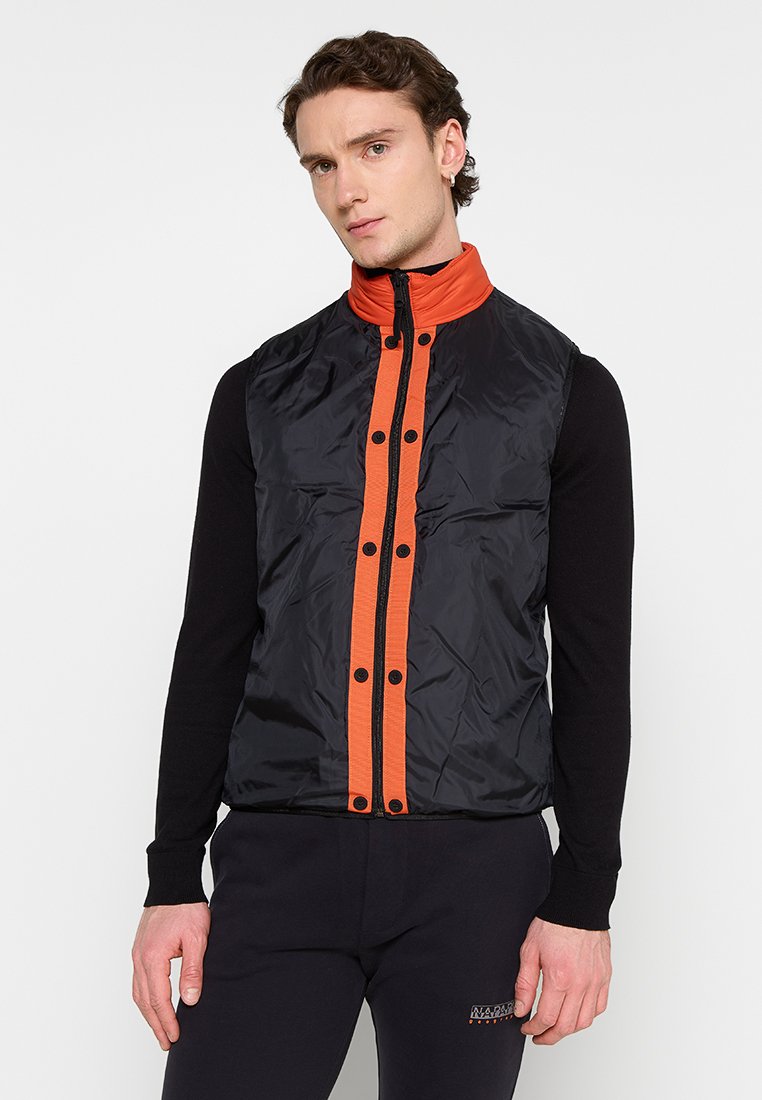 Czarna bezrękawnik z pomarańczowymi suwakami i guzikami, z wysokim kołnierzem. Materiał wydaje się błyszczący, gładki, o lekkiej konstrukcji.