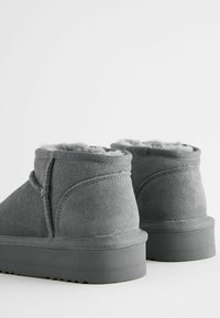 Graue Wildleder-Stiefeletten mit weicher Innenausstattung, leicht abgerundeten Schafthöhen und dicken Gummisohlen mit strukturiertem Grip-Muster.