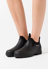 Black waterproof ankle boots with a textured finish, elastic side panels, and a pull tab. Features a sturdy rubber sole for traction.