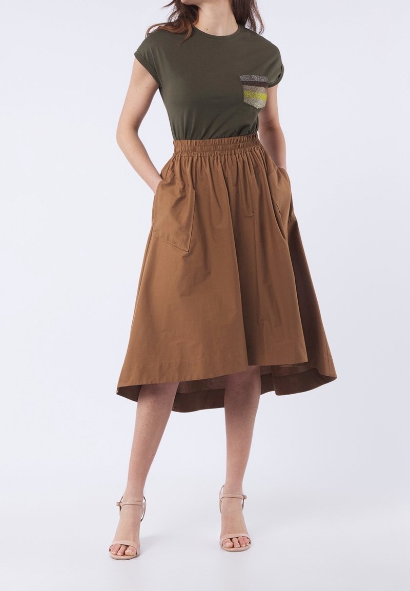 T-shirt vert olive avec une poche ornée de rayures jaunes et argentées, associé à une jupe marron jusqu'au genou avec une taille élastique et des poches.