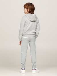 Felpa con cappuccio grigia e pantaloni della tuta abbinati, realizzati in tessuto morbido, con polsini elastici e una vestibilità casual, abbinati a sneakers bianche.