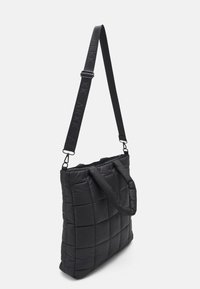 Svart quiltad tote-väska med strukturmönster, med två handtag och en justerbar rem. Dragkedjestängning upptill.