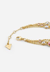 Gold-tone multi-chain bracelet featuring various round stones in pink and clear, with a triangular charm and lobster clasp closure.