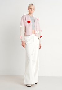 Ανοιχτό ροζ πλεκτό ζακέτα με εφαρμογές λουλουδιών, συνδυασμένη με γκρι κοντομάνικο τοπ και λευκά παντελόνια με φαρδιά πόδια. Απαλή υφή, χαλαρός σχεδιασμός.