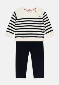 Sweater en maille avec des rayures bleu marine et blanches, doté de boutons sur les côtés et d'un col rond, associé à un pantalon uni bleu marine.