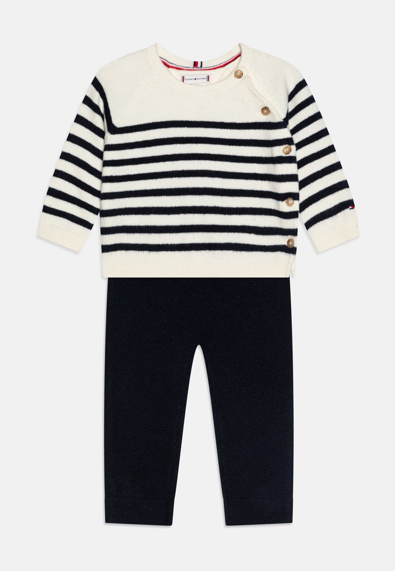 Sweater en maille avec des rayures bleu marine et blanches, doté de boutons sur les côtés et d'un col rond, associé à un pantalon uni bleu marine.