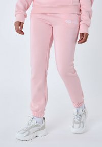 Pantalones de chándal rosas hechos de una tela suave, con cinturilla y puños elásticos, y un pequeño logo blanco cerca de la cadera.