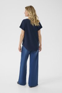 Jūras zila, īsām piedurknēm blūze ar acu dizainu, apvienota ar platām zila džinsa biksēm. Tekstūrēta auduma, brīvs piegriezums un izliekta apakša.