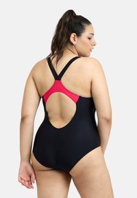 Maillot de bain noir avec des accents rouges, présentant un design dos nageur et un dos ouvert. Fabriqué à partir d'un tissu lisse, il a une silhouette ajustée.