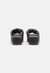 Sandales à plateforme noires avec des lanières en vinyle torsadé, texture tissée sur la semelle et une base noire unie. La vue arrière montre des talons carrés bas.