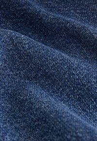 Tissu en denim bleu foncé avec une surface légèrement texturée, présentant de subtiles variations de couleur et un drapé doux et flexible.