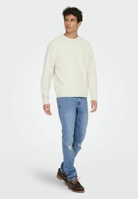 Pull crème clair à col rond, assorti à un jean bleu clair déchiré et des bottes marron à lacets. Texture lisse, coupe décontractée.