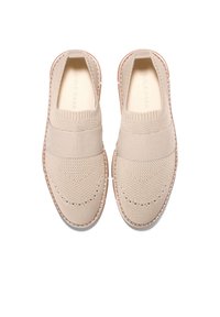 Beige Slipper mit einem gestrickten Obermaterial, elastischem Band über dem Mittelfuß und einer kontrastierenden Gummisohle. Strukturiertes Detail an der Zehe.