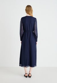 Long navy dress with sheer sleeves, elastic waist, and button accents on sleeves. Skirt falls to mid-calf, smooth texture, simple design.