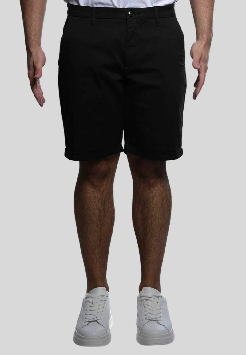 Pantaloni corti neri con taglio dritto, orlo risvoltato, tasche frontali e chiusura a un bottone, abbinati a sneakers bianche.