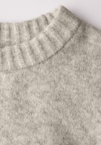 Ljust grått stickat tröja med en ribbad krage, mjuk textur och en sömlös kropp med ett subtilt mönster över hela.