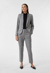 Grijs geruit pak met een getailleerde blazer en slim-fit broeken. Draag het over een zwarte coltrui. Kenmerkt zich door puntige zwarte instapschoenen.