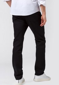 Pantalones negros de mezcla de algodón, con un corte ajustado, diseño de cinco bolsillos y sutiles detalles de costura, combinados con zapatillas blancas.