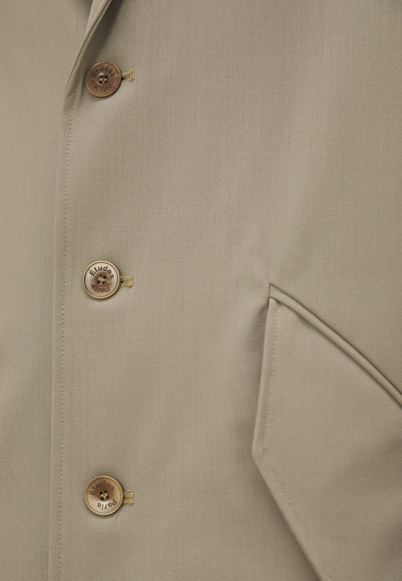 Beige Blazer mit glatter Textur, ausgestattet mit vier runden Knöpfen, einem Reverskragen und einer seitlichen Taschendetail.
