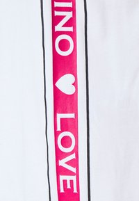 Vit tyg med en vertikal rosa rand som har texten "LOVE" och "INO" i feta, vita bokstäver, framhävd av tunna svarta kanter.