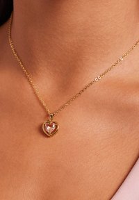Gouden ketting met een hartvormige hanger voorzien van een heldere edelsteen, gezet in een glad metalen frame, hangend aan een fijne ketting.