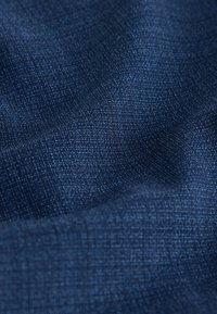 Tissu texturé bleu foncé avec un léger éclat, présentant un motif tissé qui ajoute de la profondeur et de la dimension au matériau.