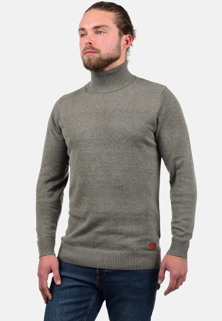 Pull en col roulé gris en tissu tricoté avec des poignets et un ourlet côtelés. Présente une petite étiquette en cuir marron sur le bas à l'avant.