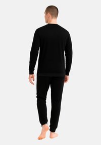 Completo in cotone nero con maglia a maniche lunghe e pantaloni, caratterizzato da un design semplice con polsini e orli a coste, visto da dietro.