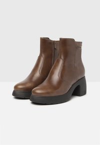 Stivaletti in pelle marrone con una finitura liscia, chiusura con zip laterale e zeppa nera spessa. Dettagli a cucitura sui lati.