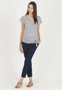 Striped short-sleeve top with a knotted detail, paired with navy pants, featuring a relaxed fit and sandals with decorative accents.