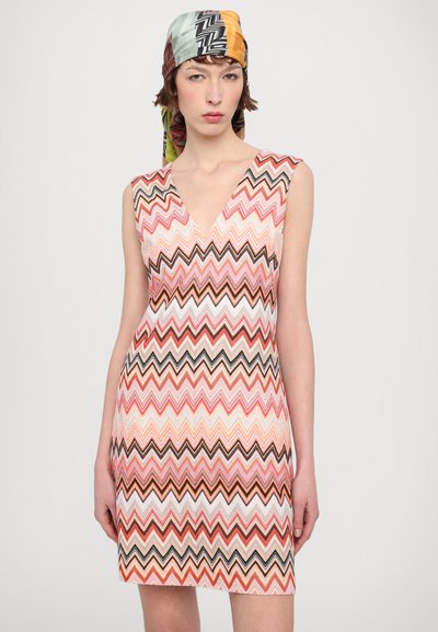 Sleeveless, V-neck dress featuring a colorful zigzag pattern in shades of pink, peach, brown, and black, complementing a patterned headscarf.