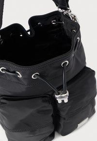 Svart nylonhinkväska med rynkad topp, silveröljetter och metallaccenter. Har två ytterfickor för extra förvaring.