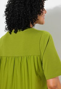Camicia verde dal taglio morbido, con un design della schiena plissettato, maniche corte e realizzata in morbido cotone. Tessuto liscio con scollo rotondo.
