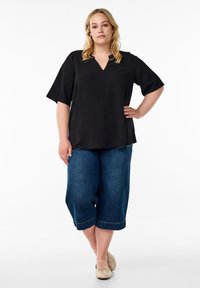 Černý top s krátkým rukávem a výstřihem do V, spárovaný s volnými tmavě modrými denimovými kalhotami culottes a béžovými balerínami. Jednoduchý design bez vzorů.
