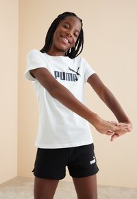 Camiseta de algodón blanca con el logo negro de "PUMA", combinada con pantalones cortos negros. Diseño suave y casual apto para ropa deportiva.