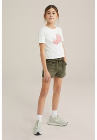 Vit bomull t-shirt med kort ärm med röda jordgubbsgraphics, ihopparat med olivgröna paperbag-shorts och ljusa sneakers.