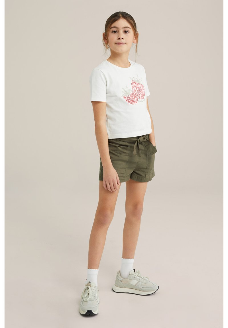 Vit bomull t-shirt med kort ärm med röda jordgubbsgraphics, ihopparat med olivgröna paperbag-shorts och ljusa sneakers.