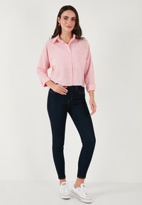 Cropped pink and white striped button-up shirt with a breast pocket, paired with dark skinny jeans and white sneakers. Smooth fabric texture.