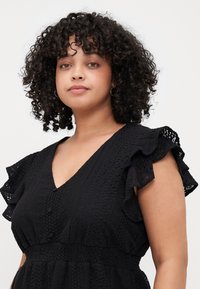 Black dress made of textured fabric, featuring a V-neck, short ruffled sleeves, and button details along the front.