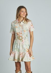 Blumenkleid aus Leinen mit kurzen Ärmeln, Knopfleiste und ausladendem Saum. Verfügt über pastellfarbene Töne, zwei Brusttaschen und einen breiten Gürtel mit einer runden Schnalle.