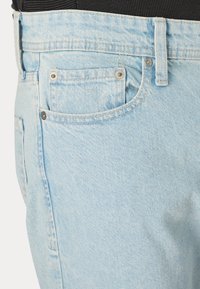Jeans de mezclilla azul claro con un diseño estándar, un bolsillo frontal, remaches de metal y un acabado sutilmente texturizado.