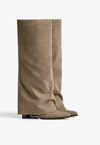 Knee-high, taupe suede boots with a soft texture, pointed toe, and a block heel; features a draped design without laces or hardware.