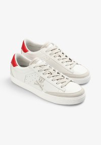 Zapatillas bajas blancas con cordones beige, pestañas en rojo en el talón, punteras de ante y logo de calavera y huesos cruzados en el lateral.
