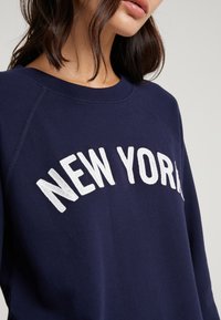 Felpa blu con ricamo bianco "NEW YORK", caratterizzata da un collo a giro e maniche raglan. Tessuto morbido con una superficie liscia.
