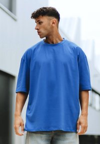 Blå överdimensionerad t-shirt i bomull, med korta ärmar, rund halsringning och en mjuk textur. Komplementeras av denimbyxor.