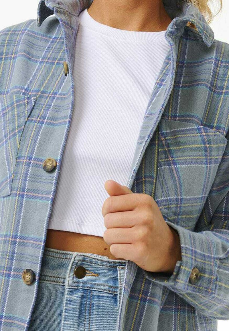 Chaqueta de franela a cuadros en tonos azul y verde con detalles de botones, con un cuello, combinada con un crop top de canalé en blanco y vaqueros de cintura alta.