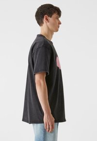 Pārāk liels melns kokvilnas t-krekls ar apaļu kakla izgriezumu, ar smalku rozā grafiku. Strukturēta auduma, pazemināti pleci un brīva piegriezuma.