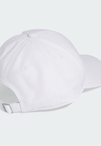 Gorra de béisbol blanca vista desde atrás con correa ajustable y hebilla de metal sobre un fondo claro uniforme.